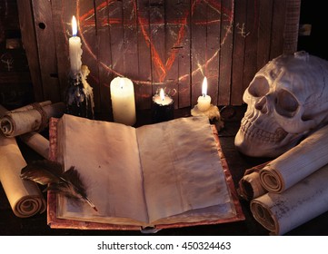 Open witch book with parchments, paper scrolls, skull and evil candles against pentagram background. Halloween concept, black magic ritual or satanic spell 