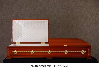 Open Wooden Funeral Casket On Stand At Grey Wall