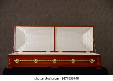 Open Wooden Funeral Casket On Stand At Grey Wall