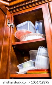 Open wooden kitchen cabinet door cupboard with many plastic containers dishes, boxes, lids cluttered on shelves closeup