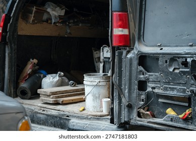 An open work van reveals construction tools, buckets, and materials inside the cargo area. The image represents manual labor, maintenance, and service work.