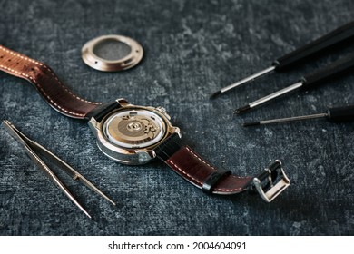 Open wristwatch, tweezers and screwdrivers, watch repair concept, close up, shallow depth of field