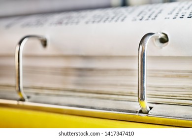 Open yellow binder close up , stack of white papers and bright metal rings , in the background black text out of focus