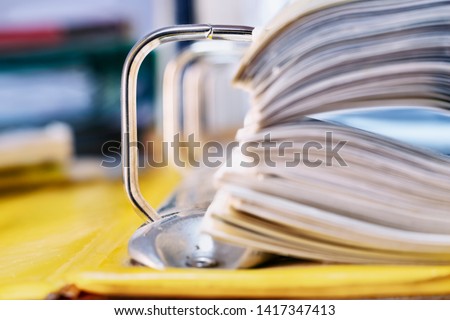Open yellow binder close up , stack of white papers and bright metal rings , in the background office folders