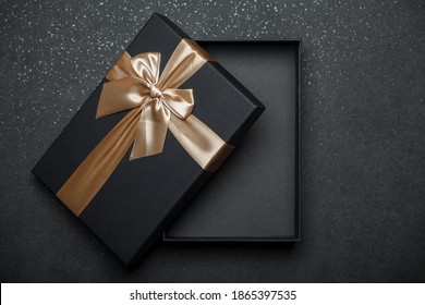 Opened Black Gift Box With Golden Ribbon And Large Bow On Dark Granite Surface. Empty Box. Layout