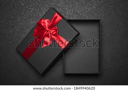 Opened black gift box with a red ribbon and a large bow on a dark granite surface. Empty box. Mockup