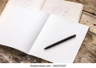 Opened blank exercise book with workbook of physics on wooden table. Student learning background