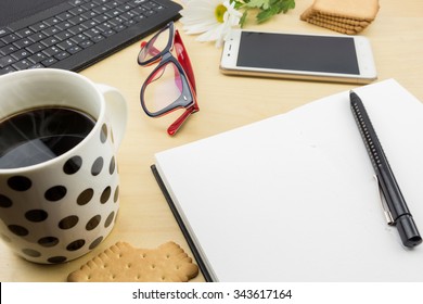 Opened blank notebook with pen, keyboard  and cup of coffee and cookies, on wooden desktop.