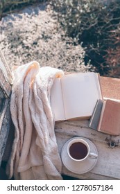 Opened Book, Cup Of Tea Or Coffee, Glasses And Knitted Sweater On Window Sill Over Blooming Tree View. Cozy Spring Weekend Concept. The Text On Pages Is Not Recognizable.