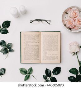 Opened book, glasses, pink roses on white background. Flat Lay