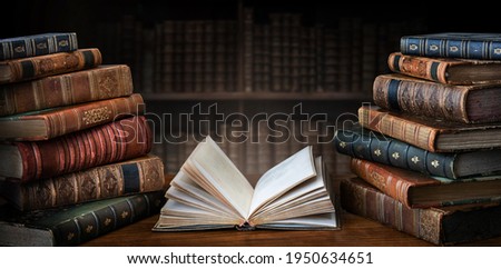 Opened book and stacks of old books on wooden desk in old library. Ancient books historical background. Retro style. Conceptual background on history, education, literature topics.