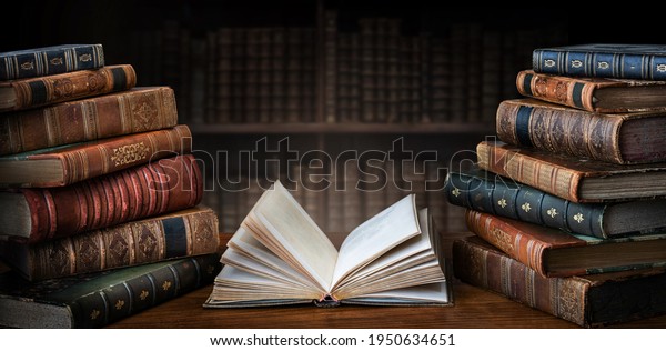 Opened book\
and stacks of old books on wooden desk in old library. Ancient\
books historical background. Retro style. Conceptual background on\
history, education, literature\
topics.\
\
