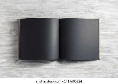 Opened booklet with blank black pages on light wooden background. Flat lay.