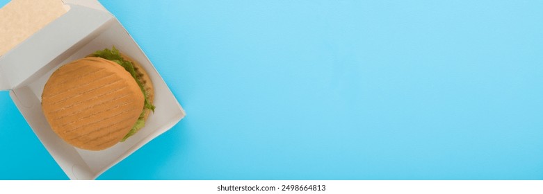 Opened carton box with fresh burger on light blue table background. Pastel color. Closeup. Fast food delivery. Wide banner. Top view. - Powered by Shutterstock