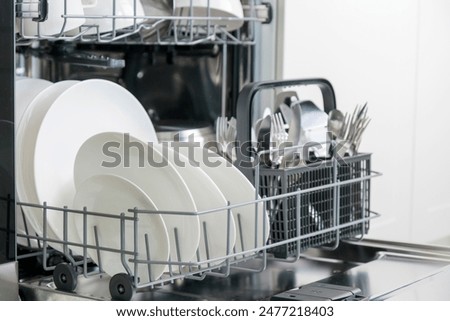 Opened dishwasher machine with clean tableware, white porcelain plates. Convenient modern technologies in the kitchen