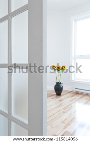 Opened door leading into a contemporary room full of light, decorated with flowers.