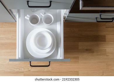 opened drawer at kitchen cupboard with white tableware set from clean plates, bowl and ceramic cups