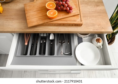 Opened drawer with set of cutlery and fresh fruits on counter in kitchen