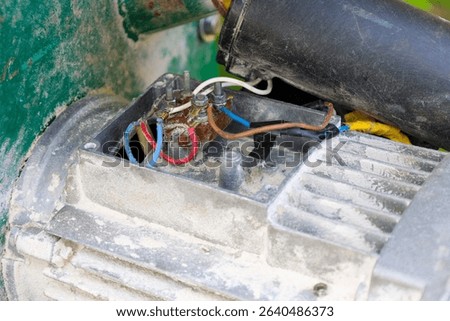 An opened electrical motor box with connected multicolored wires and terminals, indicating a repair or inspection process. Dust and signs of wear on the surface highlight the working nature of the equ