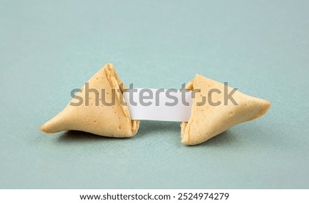 Opened fortune cookie with a empty piece of paper inside, a "fortune". Empty paper to fill in yourself. Blue color studio background.