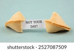 Opened fortune cookie with a piece of paper inside, a "fortune" saying: NOT YOUR DAY! Sarcastic bad luck concept. Blue color studio background.