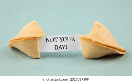 Opened fortune cookie with a piece of paper inside, a "fortune" saying: NOT YOUR DAY! Sarcastic bad luck concept. Blue color studio background. - Powered by Shutterstock