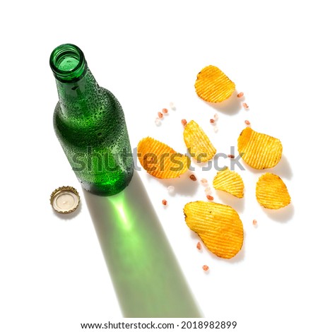 Opened green beer bottle and potato chips with himalayan salt, top view