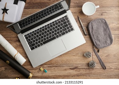 Opened Laptop On Table With Cosmetic Bag, Pine Cones And Wrapping Paper, View From Above