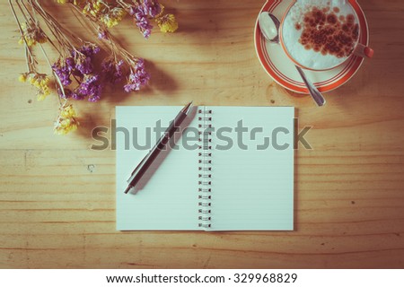 Opened notebook with blank area for text or message, pen and a cup of hot coffee on wood table in afternoon time with film filter effect