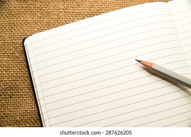 Opened notebook with a blank sheet and pencil on the old tissue