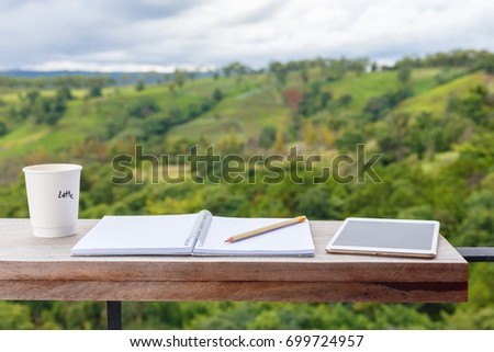 Opened notebook with cup of coffee and tablet, prepare to write at the balcony by the mountain view environment
