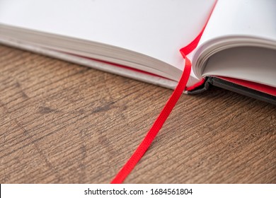 Opened Notebook With Empty Pages. Hard Laminated Cardboard Cover, Opened Book, Clear Snow White Pages, Red Fabric Bookmark. Soft Shadows And Natural Light Make It Look Like Some Snow White Surface.