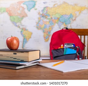 Opened Notebook And Stack Of Books On A Table With School Bookbag And World Map In Background