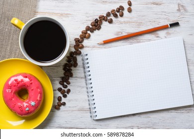Opened notepad and cup of coffee with donut on wooden table