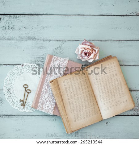 Opened old book with lace, rose and keys on shabby chic mint background, top view point