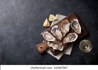 Opened oysters, ice and lemon on board and white wine on stone table. Top view with copy space
