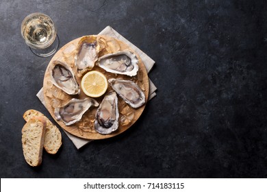 Opened oysters, ice and lemon on board and white wine on stone table. Top view with copy space