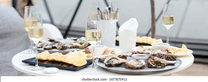Opened oysters and lemon with white wine on the table. Restaurant delicacy, beautiful table setting. Saltwater oysters dish. Romantic dinner in restaurant.