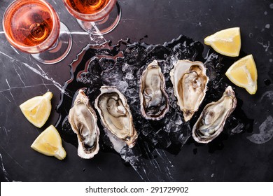 Opened Oysters on dark marble background with ice, lemon and rose wine