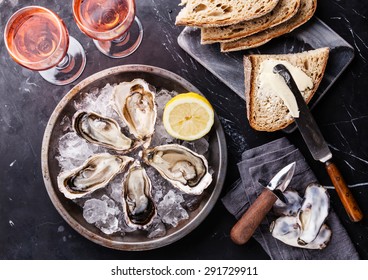 Opened Oysters on metal plate with dark bread with butter and rose wine on dark marble background 