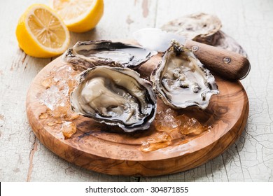 Opened Oysters on olive wood board on blue wooden background with lemon and oyster knife