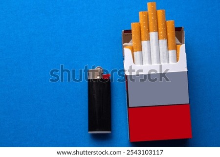 opened packet with  filtered cigarettes ,with a black lighter next to on blue background. selective focus 