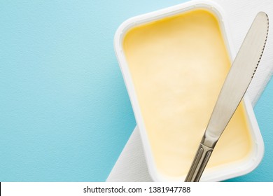 Opened Plastic Pack Of Light Yellow Margarine And Knife. Closeup. Empty Place For Text Or Logo On Pastel Blue Desk.