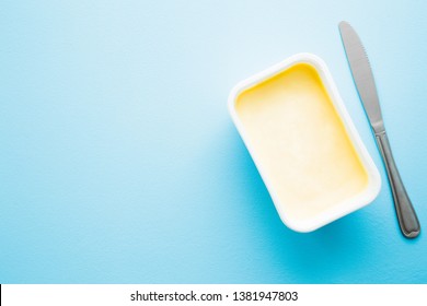 Opened Plastic Pack Of Light Yellow Margarine And Knife. Closeup. Empty Place For Text Or Logo On Pastel Blue Desk.