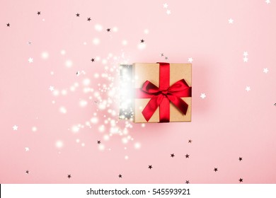 Opened Present Box With Red Bow And Magic Inside On Pink Background With Tittle Sparkles. Flat Lay Style.