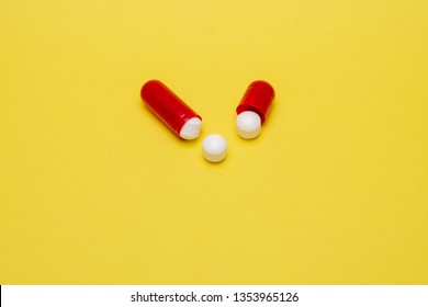 opened red capsule and three white tablets on a yellow background