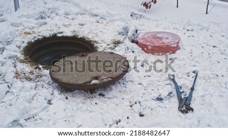 Opened Sanitary Sewer Manhole Metal Lid Cover Hatch with Plumbing Wrench Left Aside on Ground during Drainage System Maintenance on Cold Winter Day