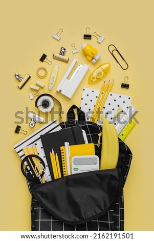 Opened School backpack with stationery on yellow background. Concept back to school. School supplies with black school bag.