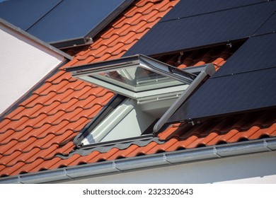 Opened skylight on a new tiled roof with solar collectors