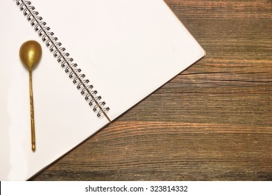 Opened Spiral Bound Notebook With Blank White Pages And Retro Vintage Golden Tea Spoon  On The Rustic Rough Brown Wooden Table